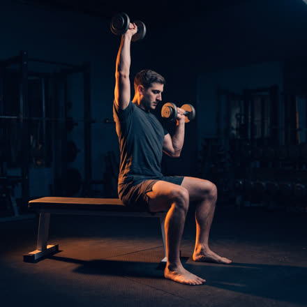 A man pressing a dumbbell overhead seated on a bench